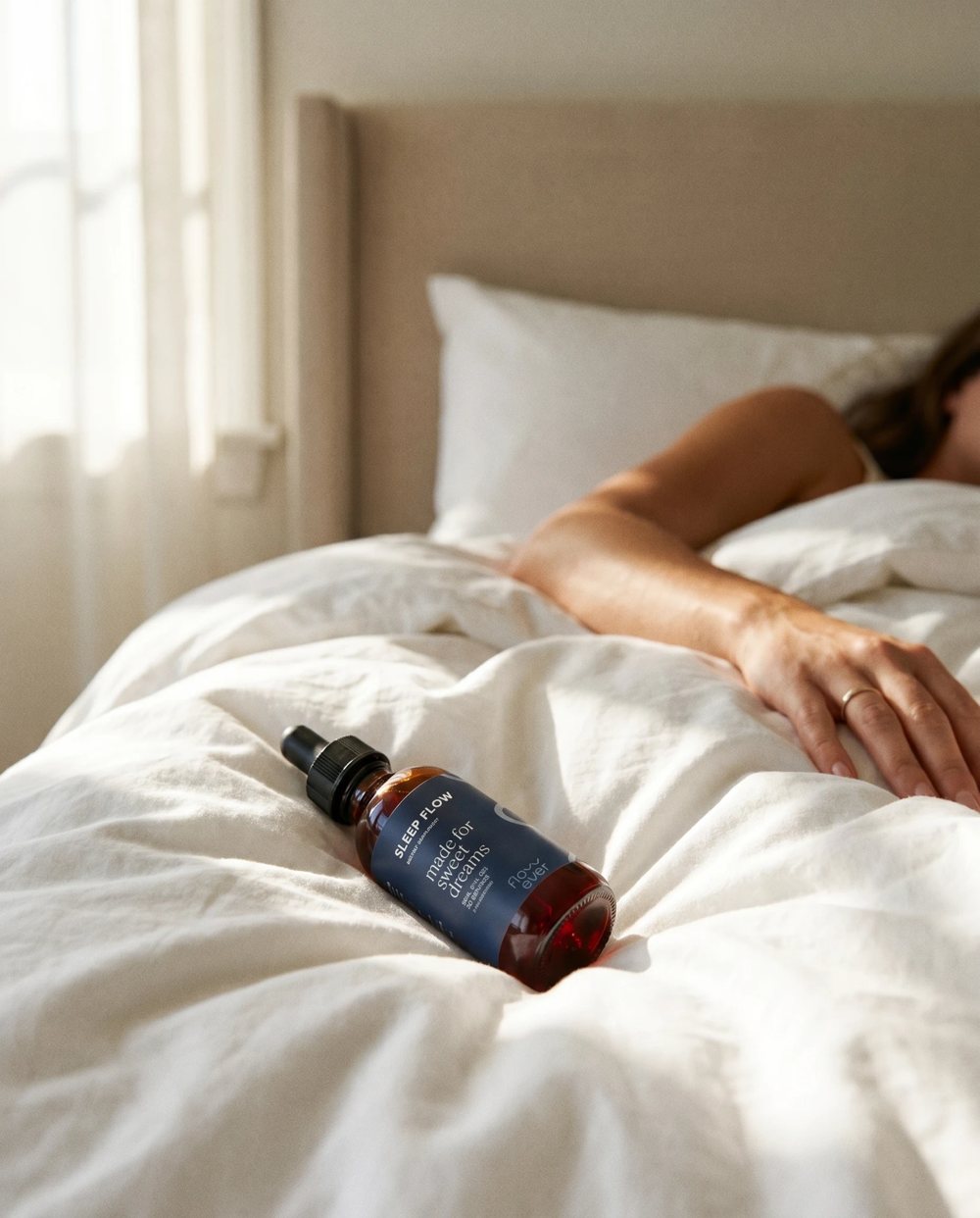 A bedroom in soft morning light with a bottle of Sleep Flow on the duvet